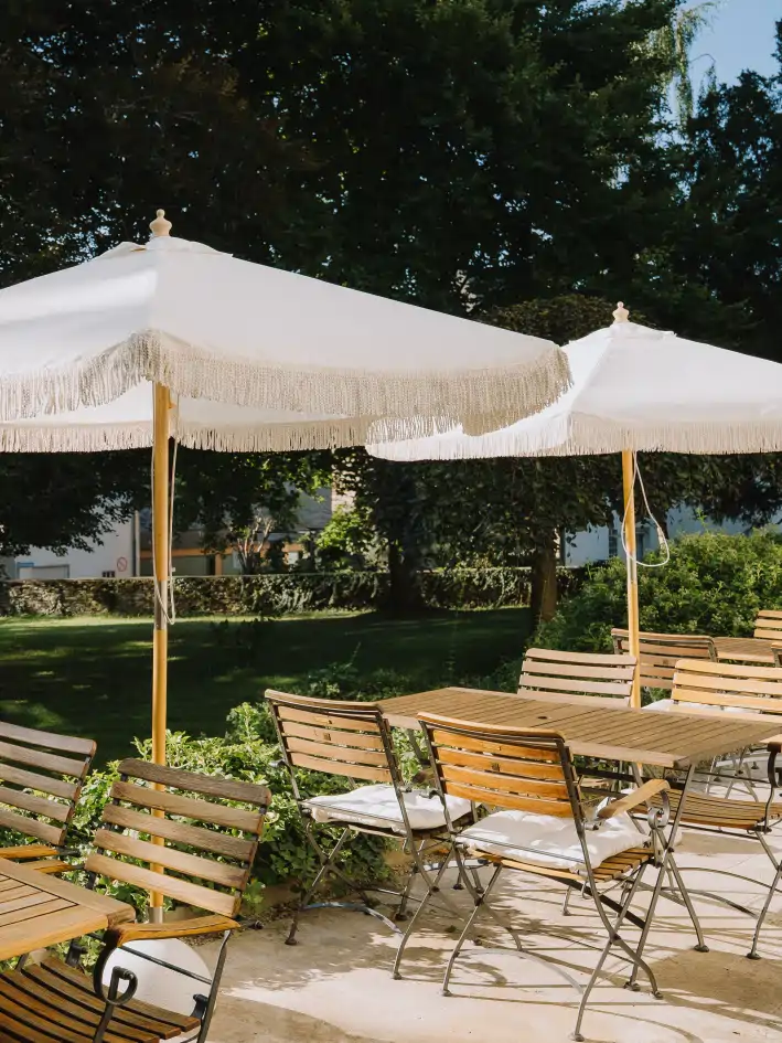 Stühle und Tische mit beigen Boho Schirmen, im Hintergrund der grüne Hotel Park
